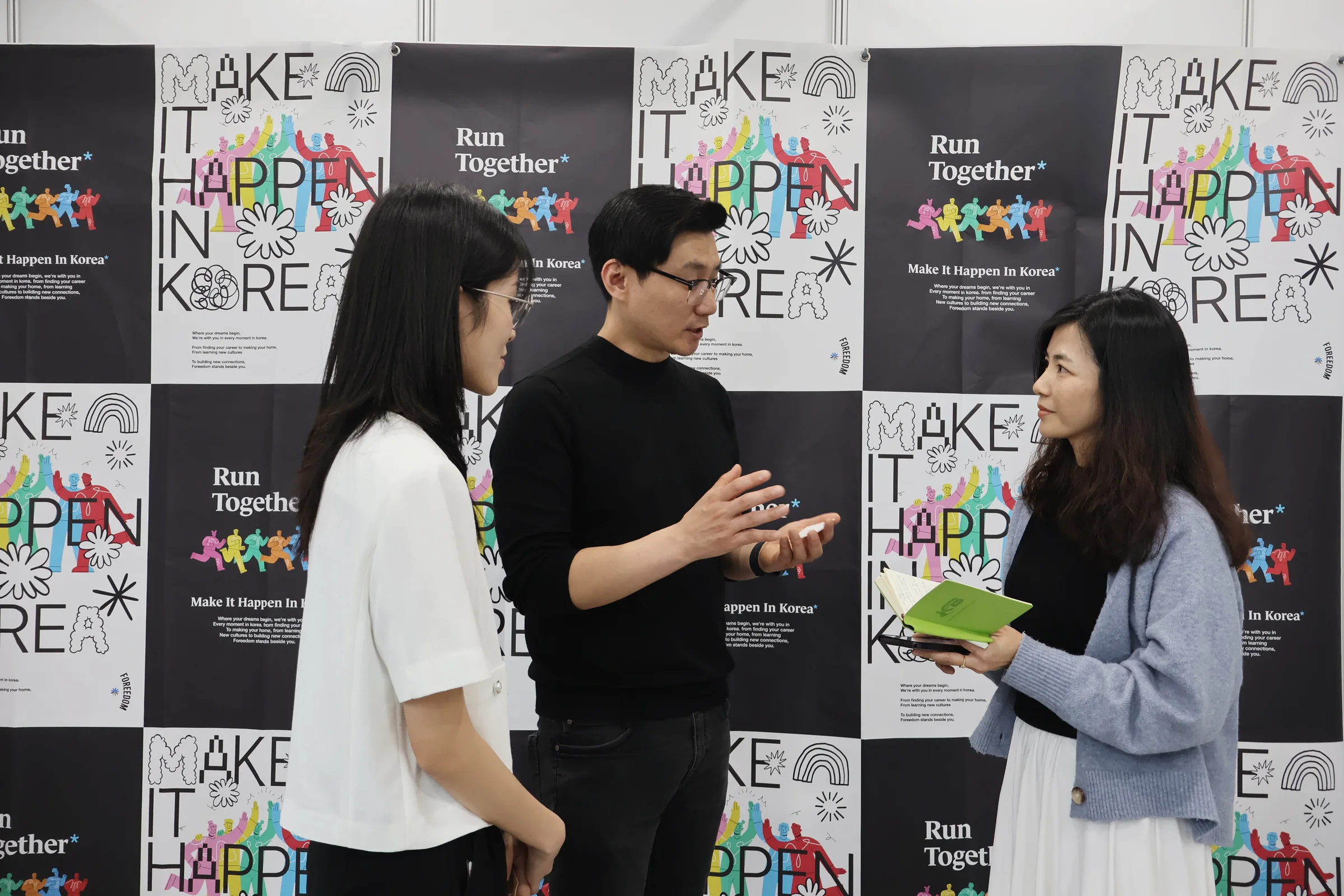 'MAKE IT HAPPEN IN KOREA' 행사 월 앞에서 자료를 들고 이야기를 나누는 유학생들.